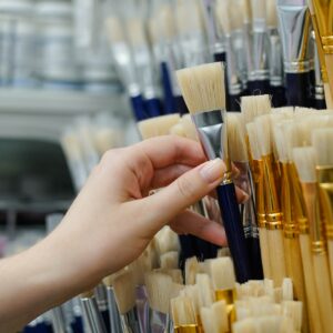Close up of woman choosing new paint brush for drawing in art store. Selling tools for artists