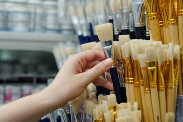 Close up of woman choosing new paint brush for drawing in art store. Selling tools for artists