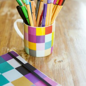 Marker and felt tip pens in desk organizer by book on wooden table