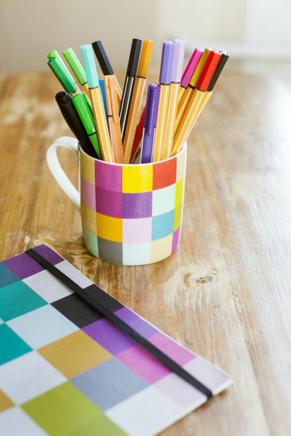 Marker and felt tip pens in desk organizer by book on wooden table